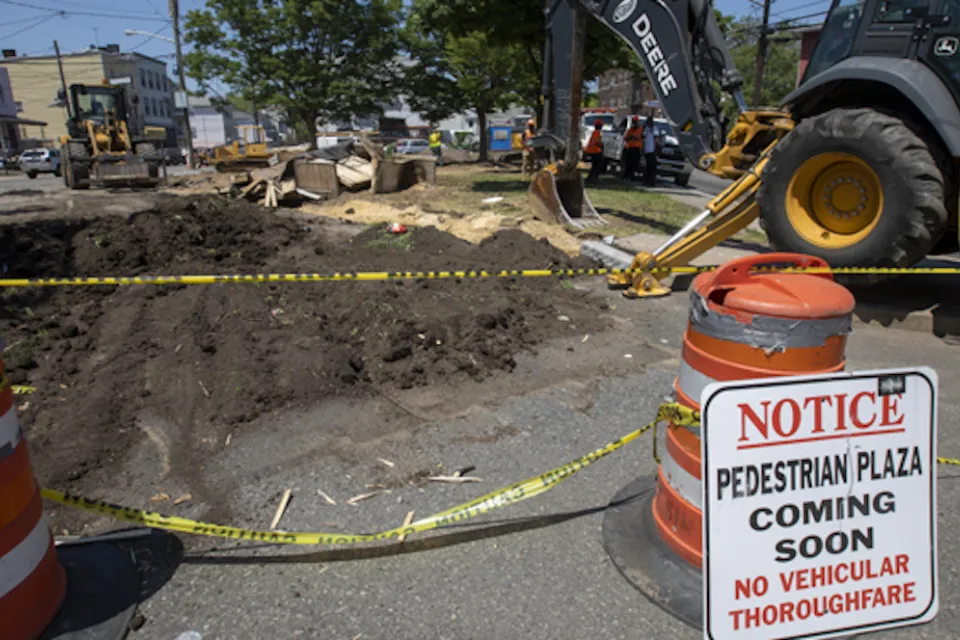 Pedestrian plaza construction site with orange cones and excavator in Jersey City, New Jersey.